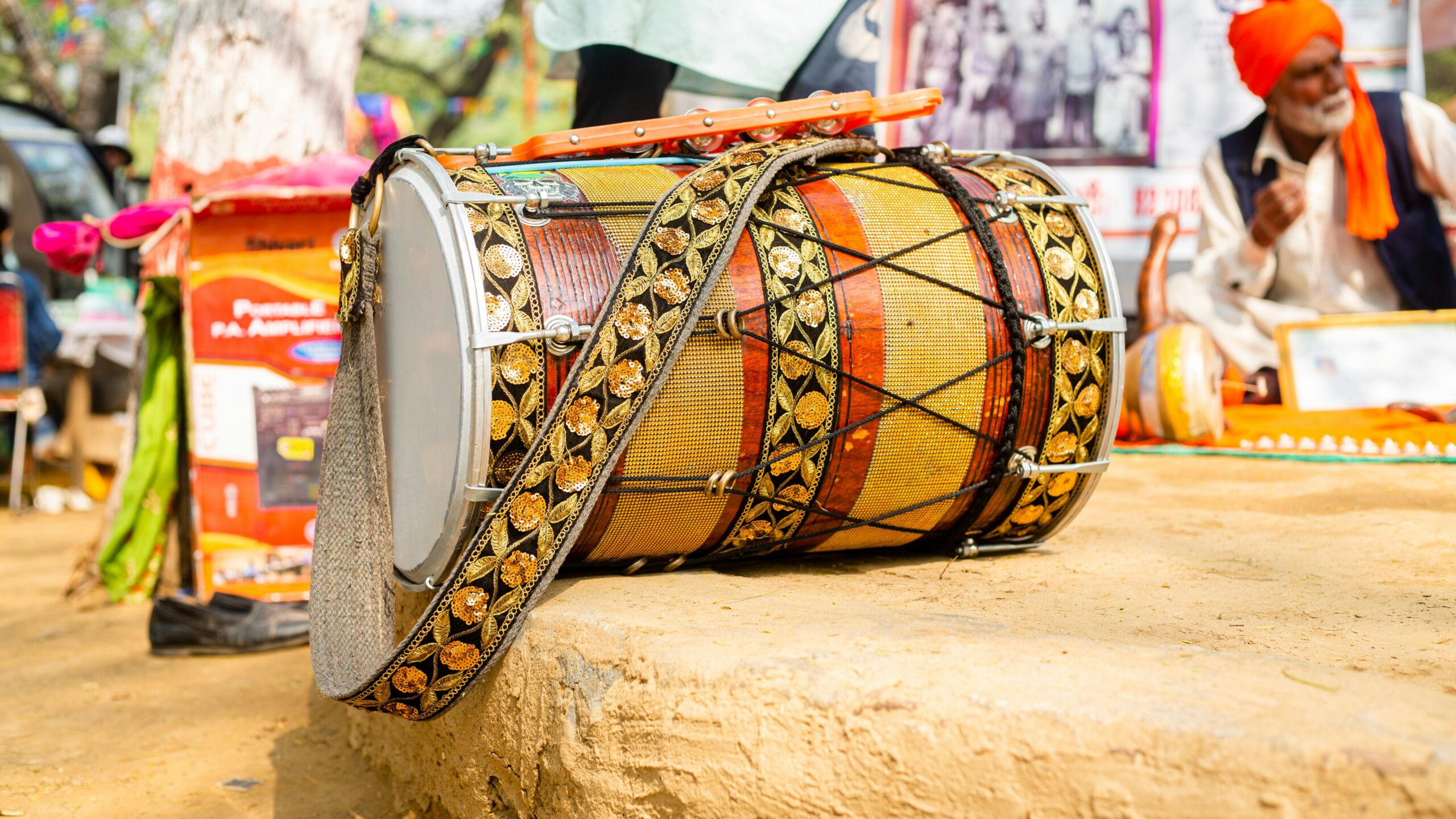 Close-up of a decorated dhol drum at an outdoor cultural event with people in the background.
